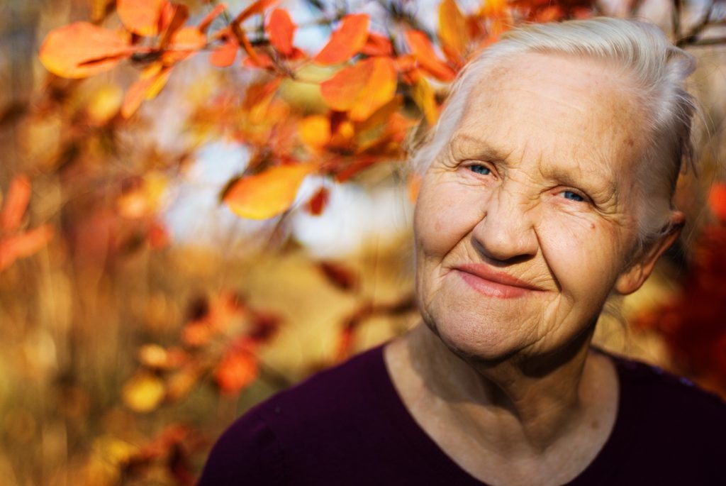 Older woman with grey hair standing in front of orange leaves